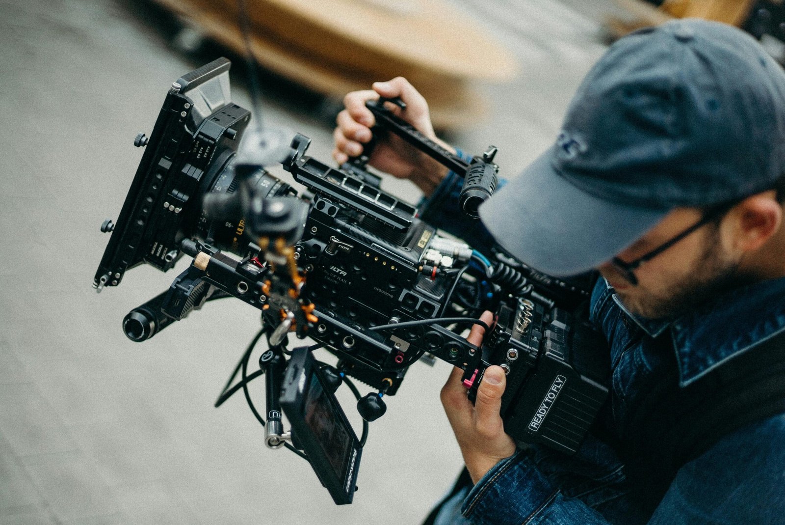 A man with a cap operates a professional video camera outdoors during daytime, capturing cinematic footage.
